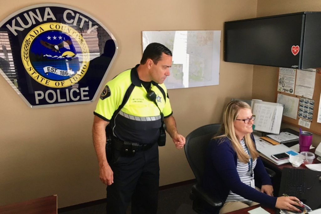 A cop and a woman looking at a computer screen with Kuna City Police logo behind them